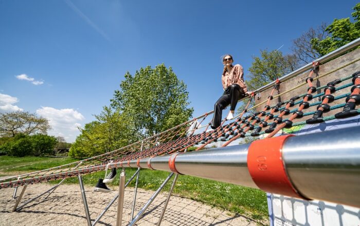 Eine Besucherin sitzt auf dem geschwungenen Klettergerüst der Station Strahlstrom. © Stadt Offenbach / Frank Rumpenhorst